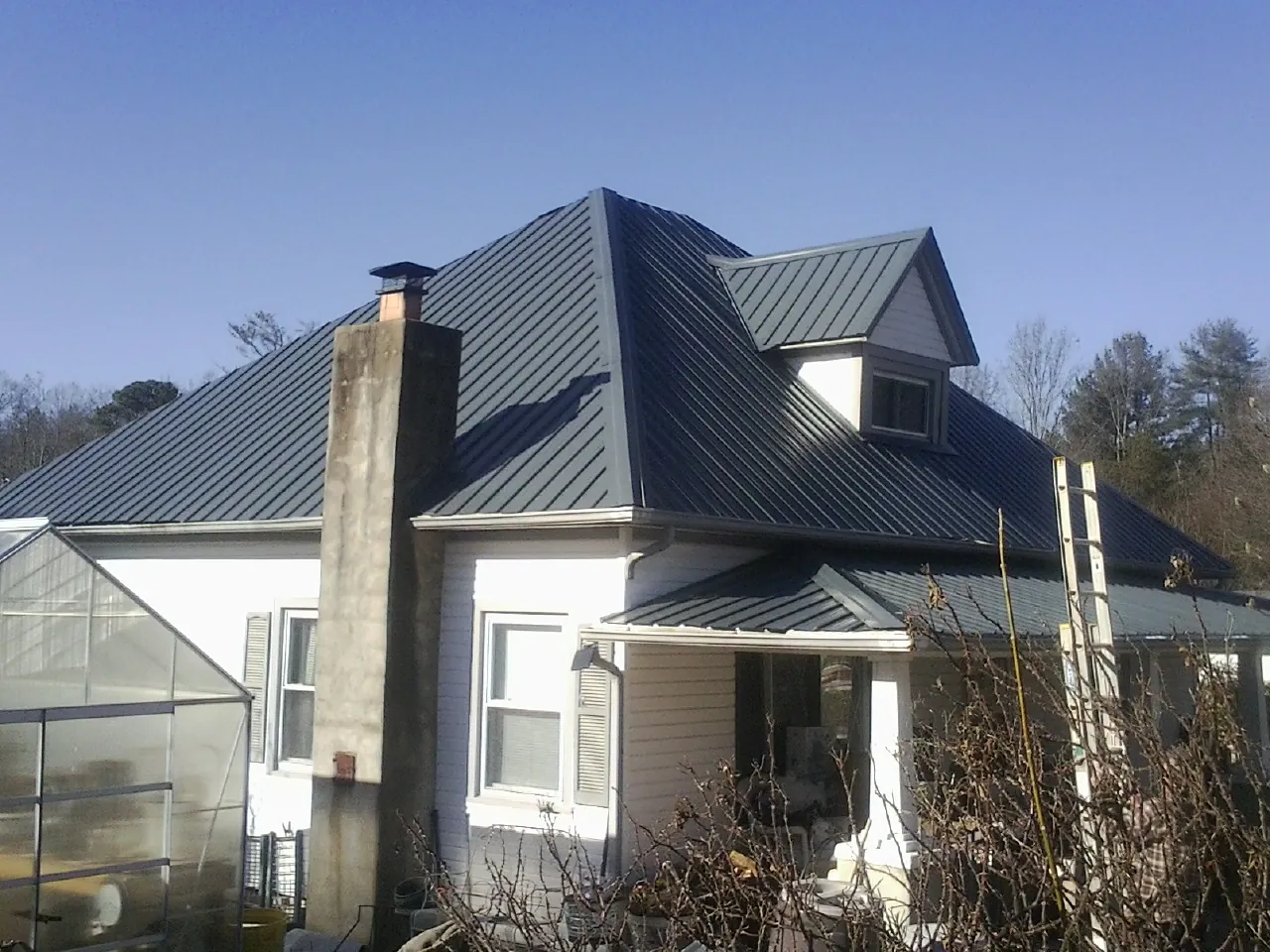 Dark blue standing seam metal roof on a white farmhouse with dormer — Slate & Tile Roof Repair by Roofing Brothers in Aledo