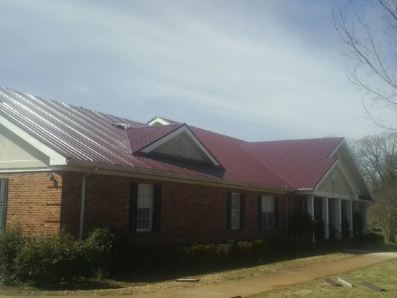 Red metal roof with gabled entries on a long brick building, from a Hail Damage Roof Repair job in Aledo