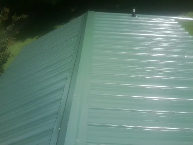 New green metal panels meeting at the ridge of a roof — Flat Roof Repair work by our crew in Aledo