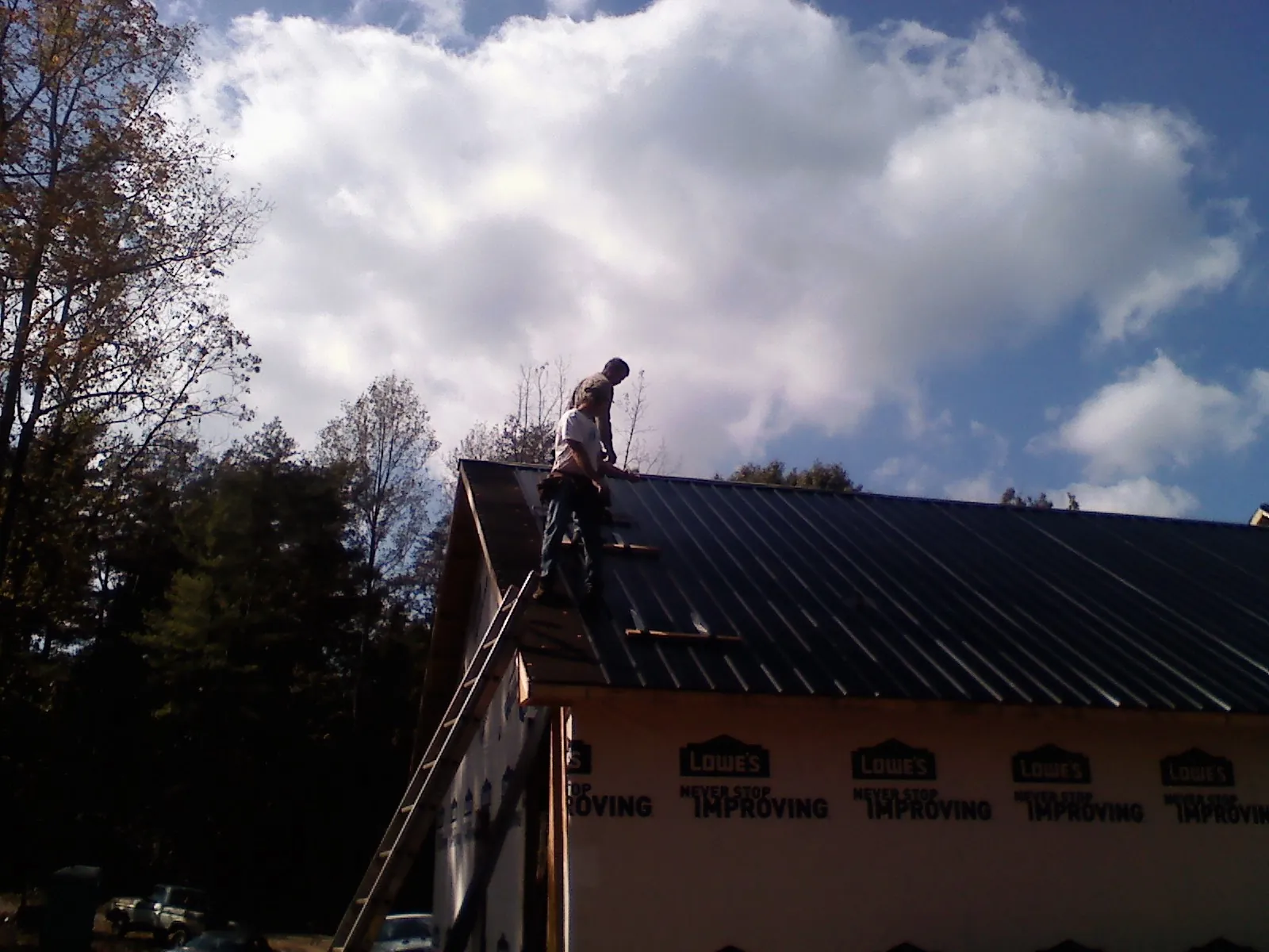 Roofer fastening dark metal panels high against a cloudy sky, from a Roof Inspection job in Aledo