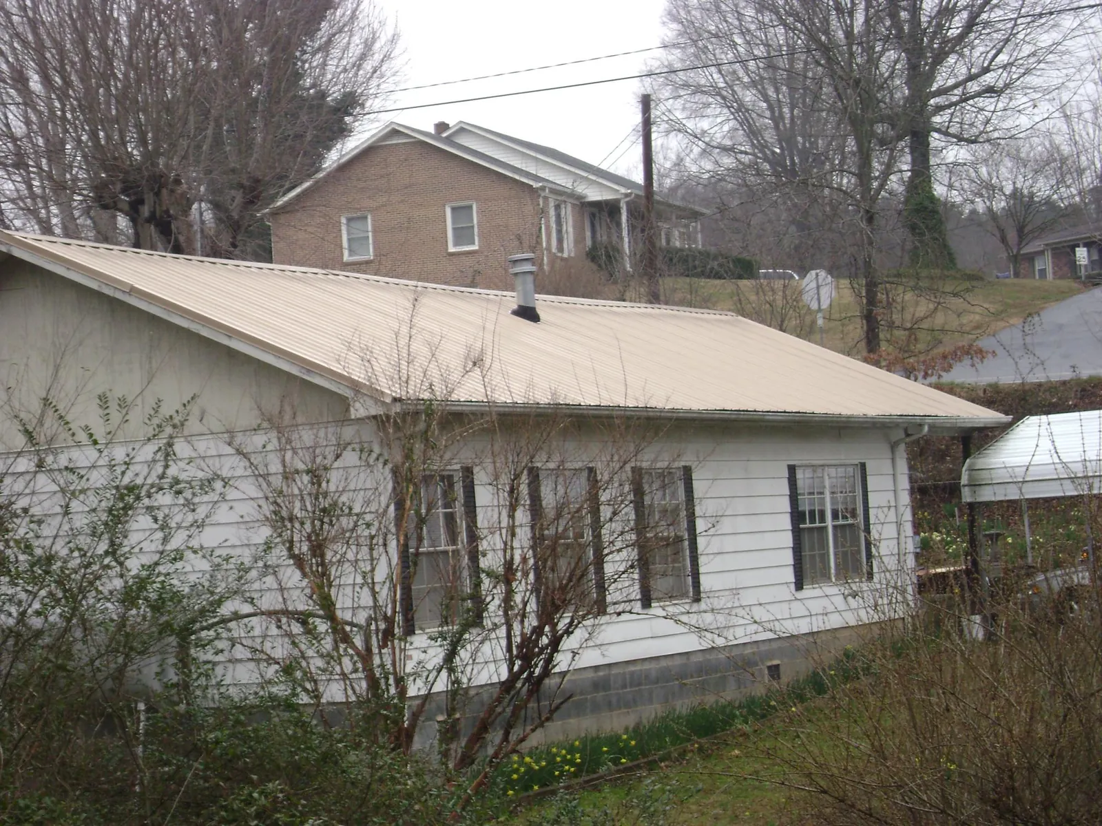 Tan metal roof on a white sided house set into a hillside — Commercial Roofing by Roofing Brothers in Aledo